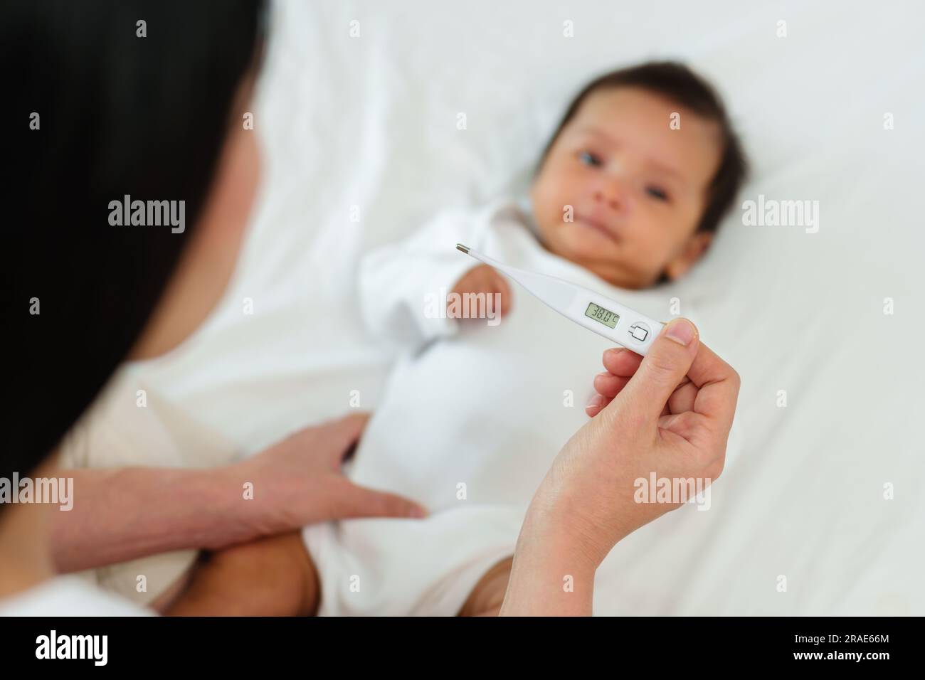 mother measuring high temperature with thermometer of ill baby on a bed Stock Photo