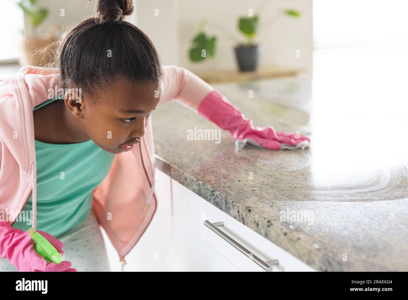 African american girl wearing pink rubber gloves cleaning countertop in kitchen Stock Photo