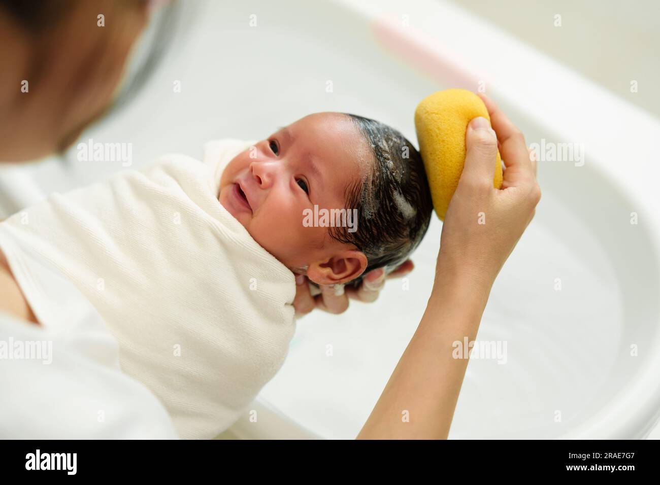 mother is washing newborn baby hair with sponge in a bathtub Stock