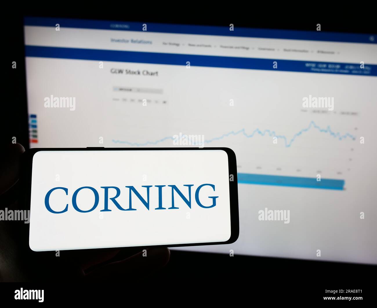 Person holding mobile phone with logo of American technology company Corning Incorporated on screen in front of web page. Focus on phone display. Stock Photo