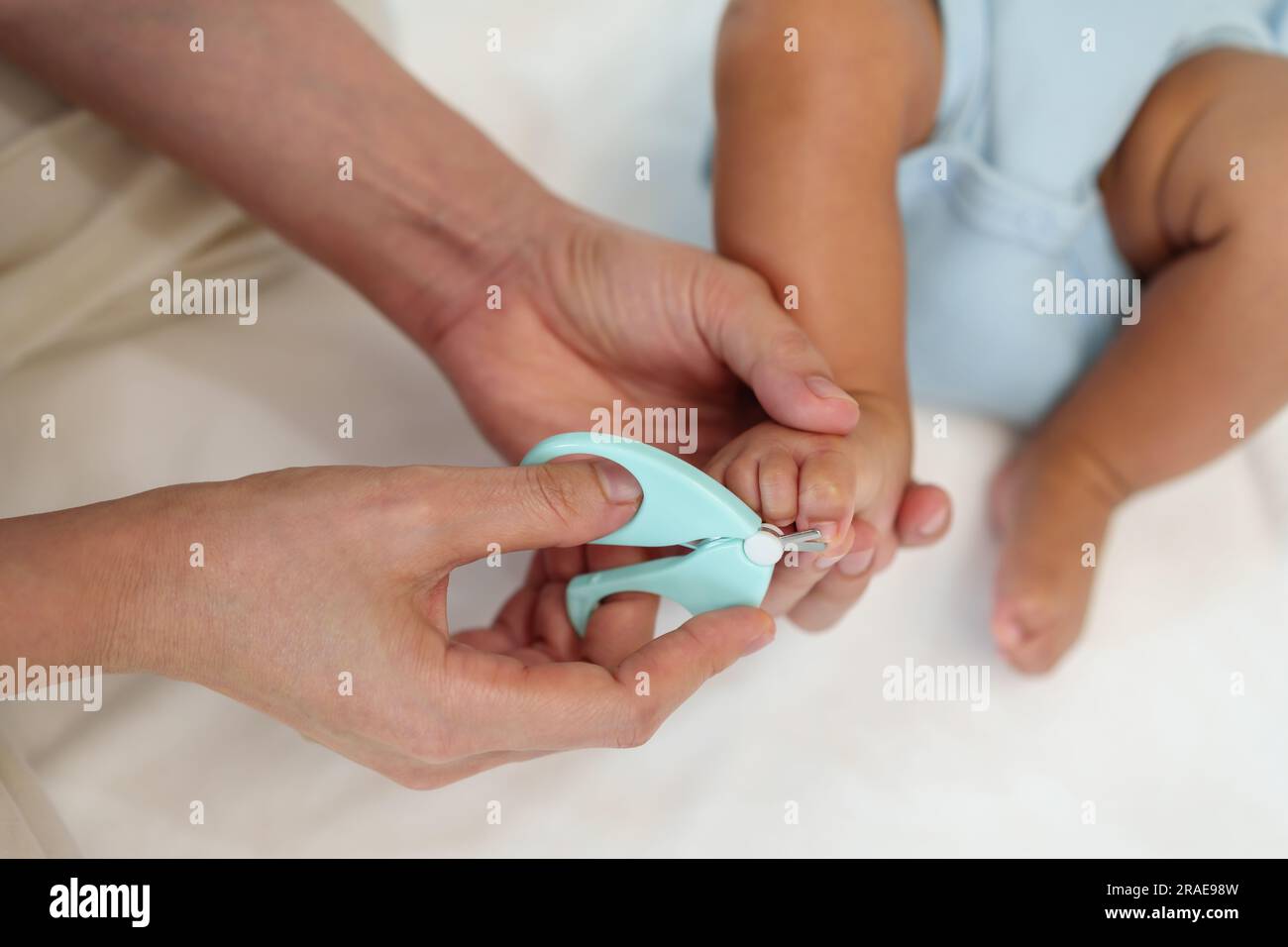 mother cutting newborn baby's foot fingernails with nail scissors Stock