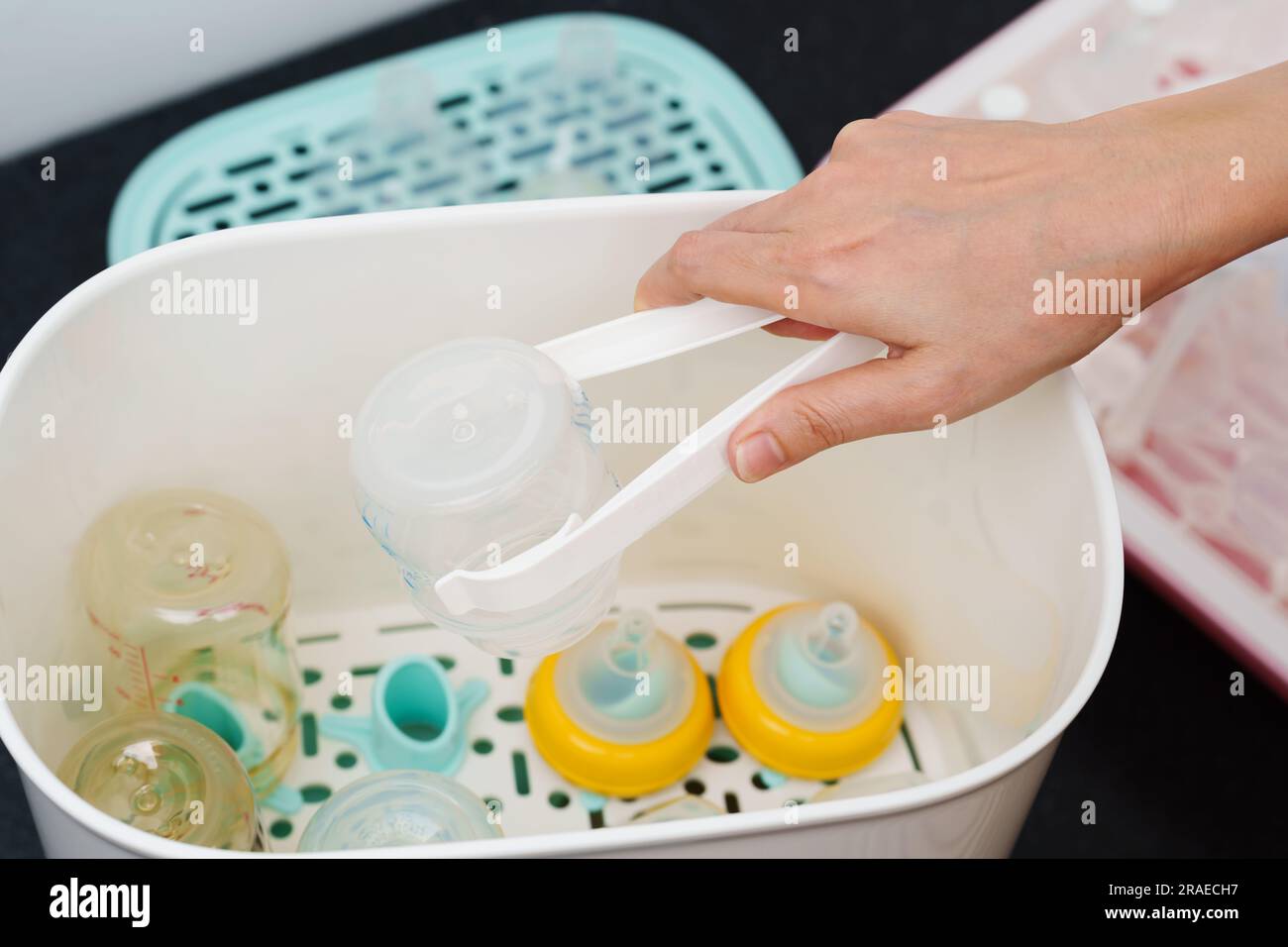 hand of mother feeding baby milk bottle into the Steam sterilizer Stock