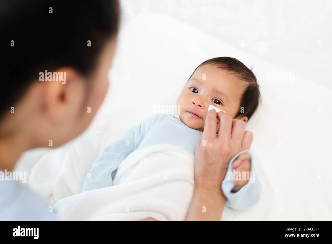 mother cleaning and wiping newborn baby face with cotton pad on a bed Stock Photo Alamy