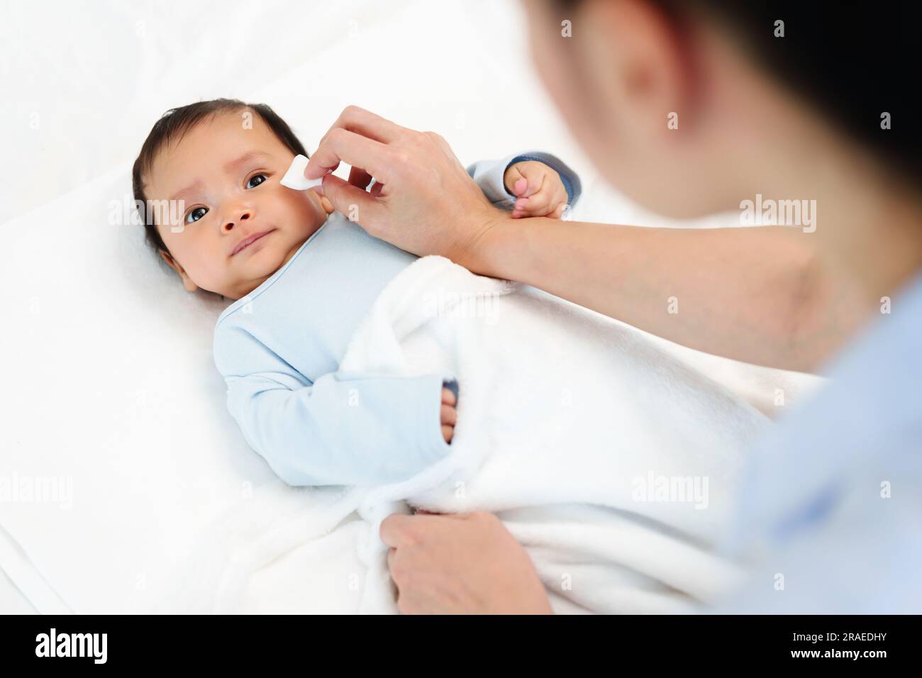 mother cleaning and wiping newborn baby face with cotton pad on a bed Stock Photo Alamy
