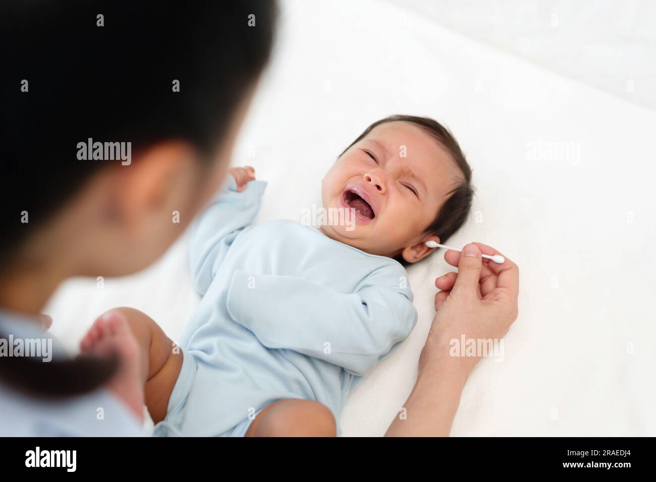 mother using cotton bud to cleaning ear of crying newborn baby on a bed