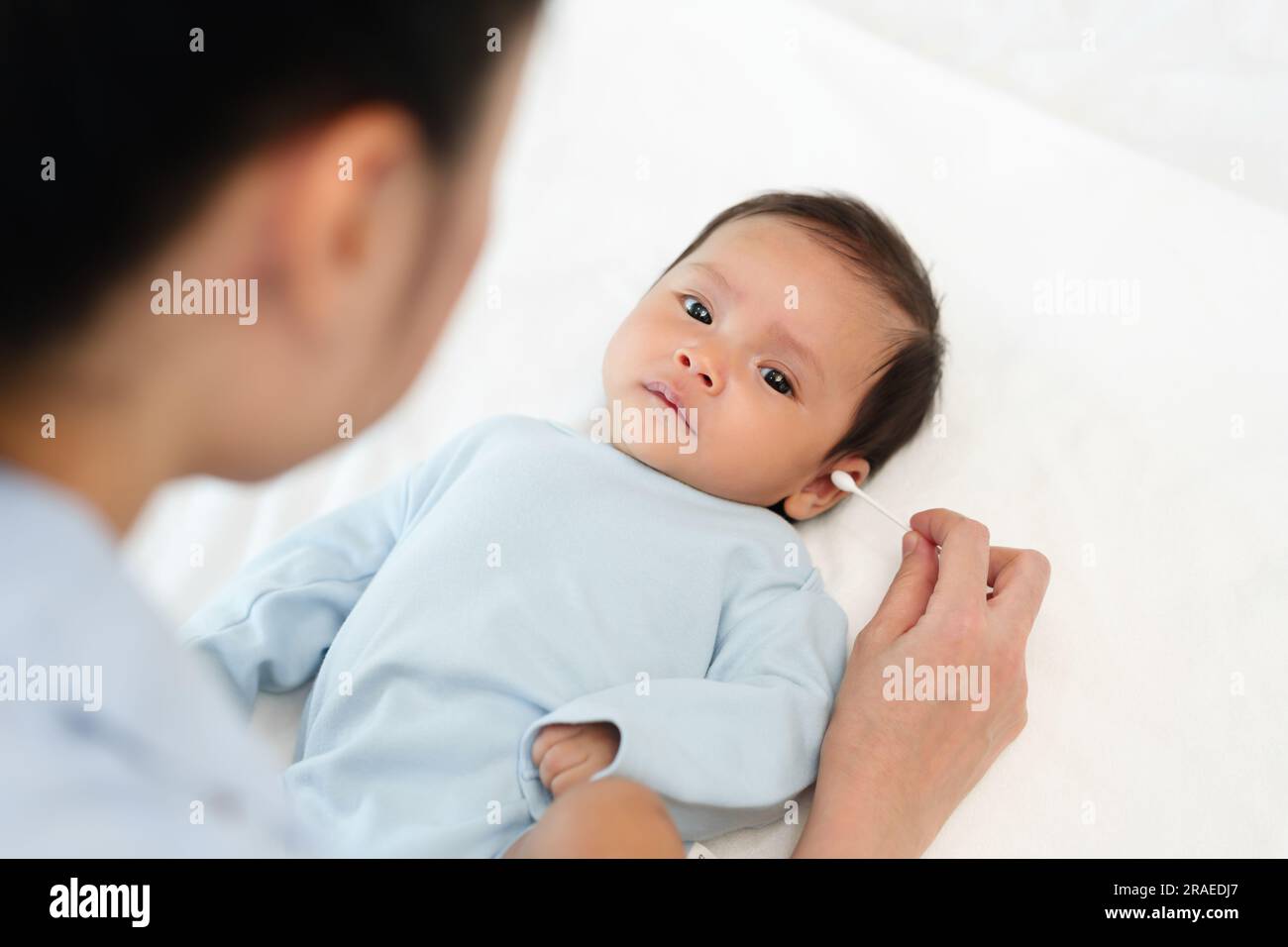mother using cotton bud to cleaning ear of newborn baby on a bed Stock