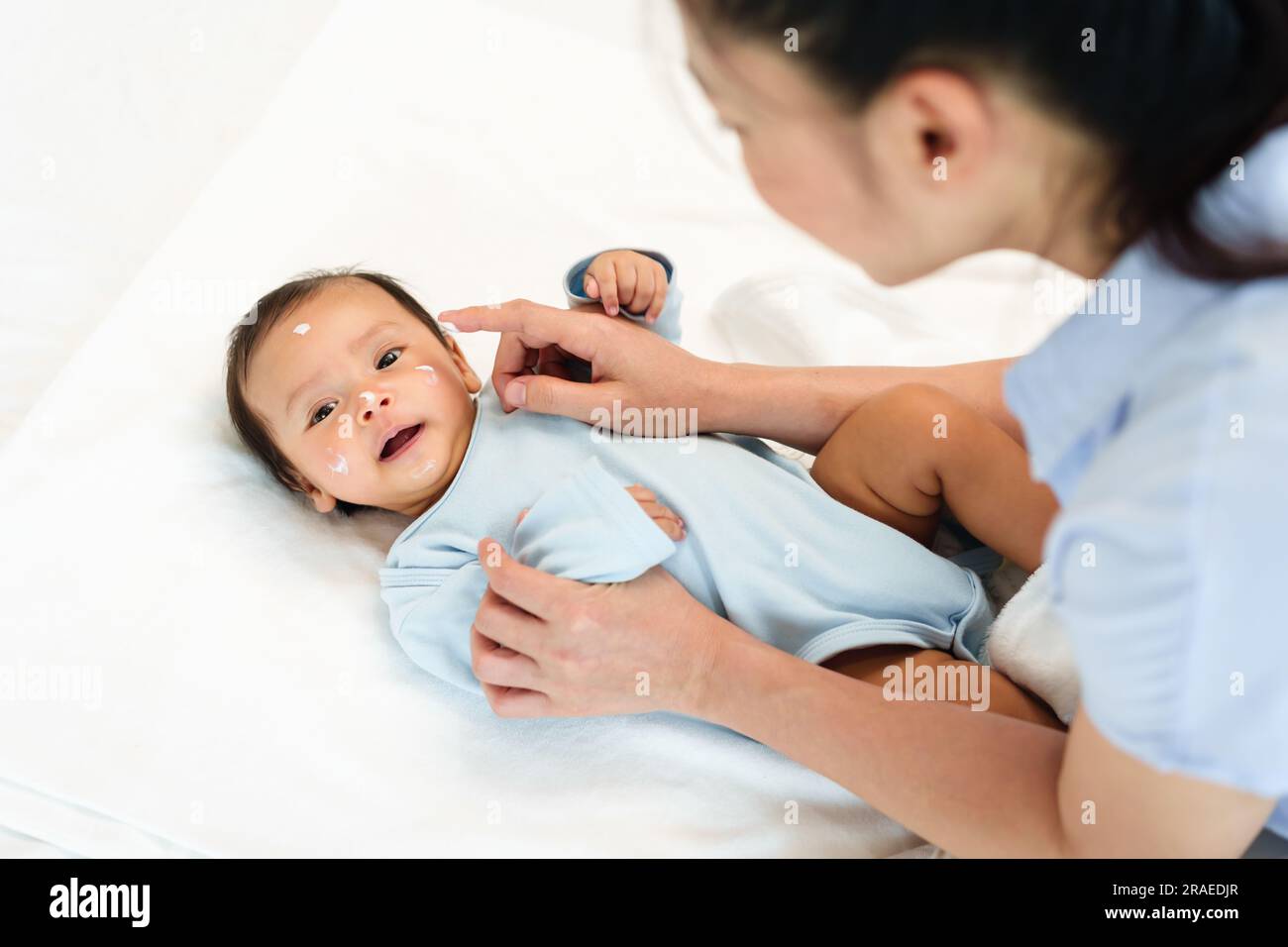 mother applying moisturizing cream on face of her newborn baby Stock