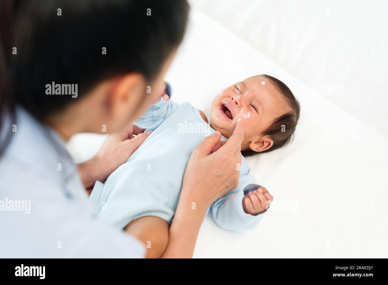 mother applying moisturizing cream on face of her newborn baby Stock