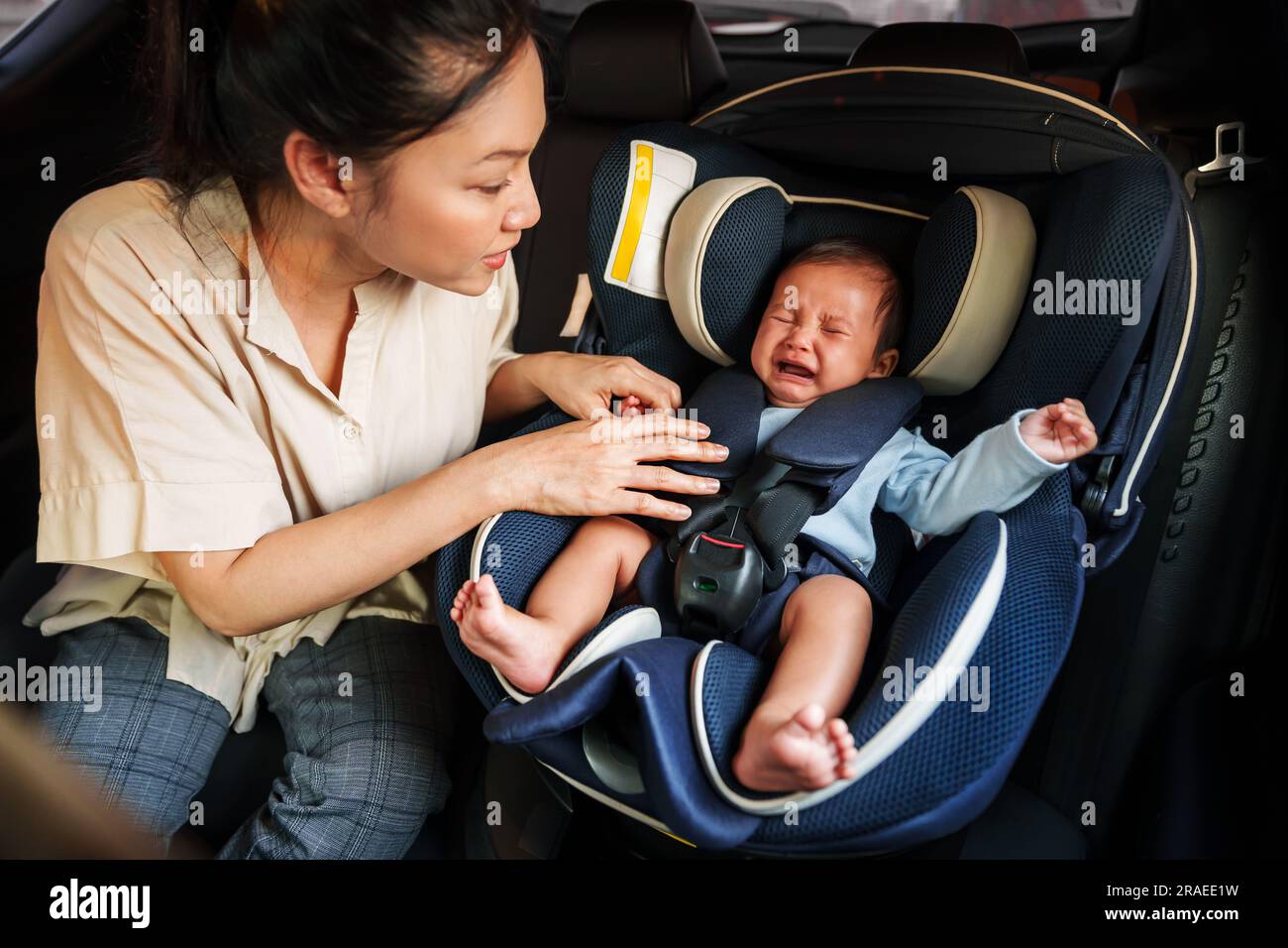 mother consoling her newborn baby crying while putting and fasten seat