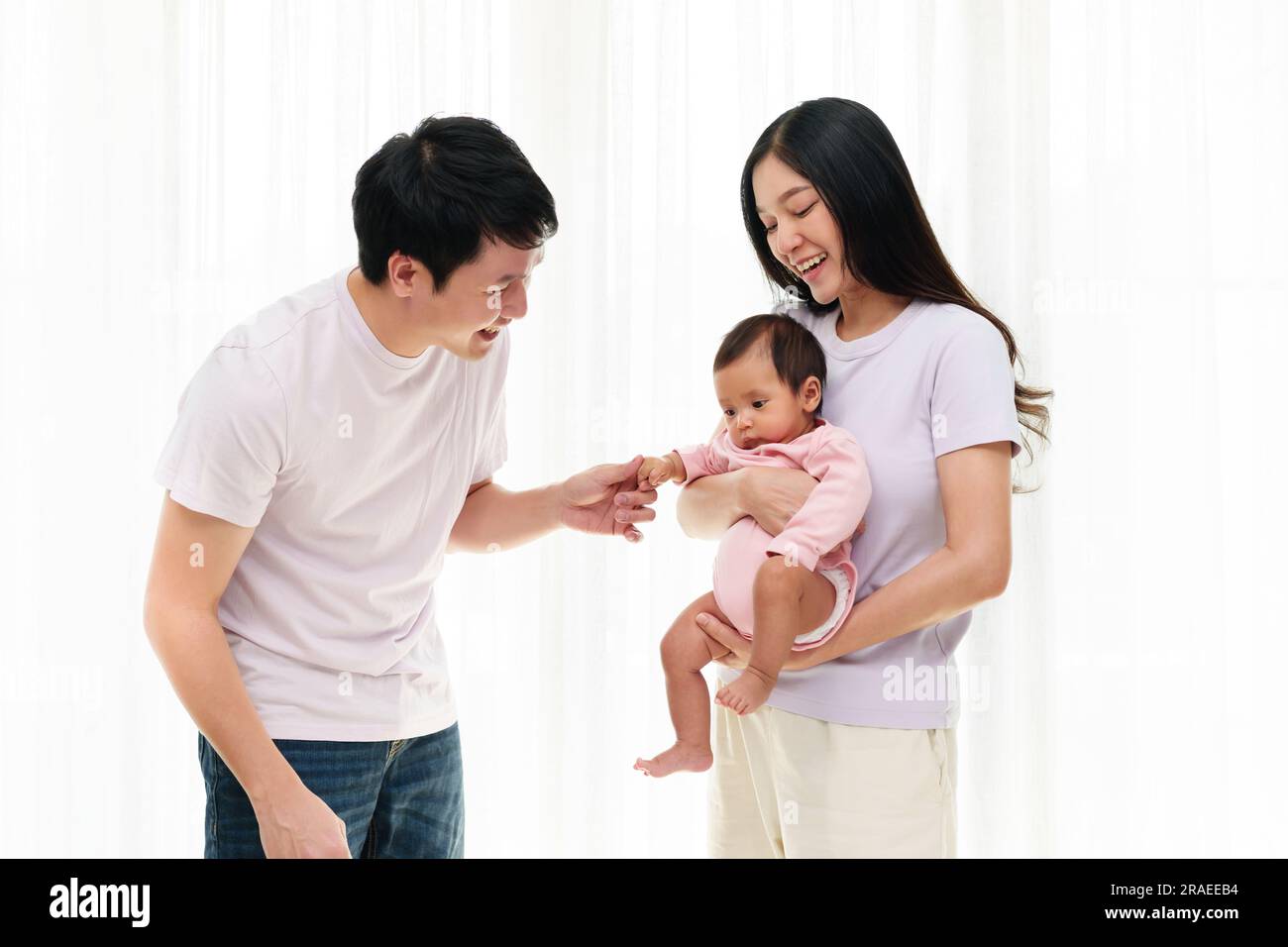 cheerful father and mother holding and playing with newborn baby on white window background. happy family concept Stock Photo