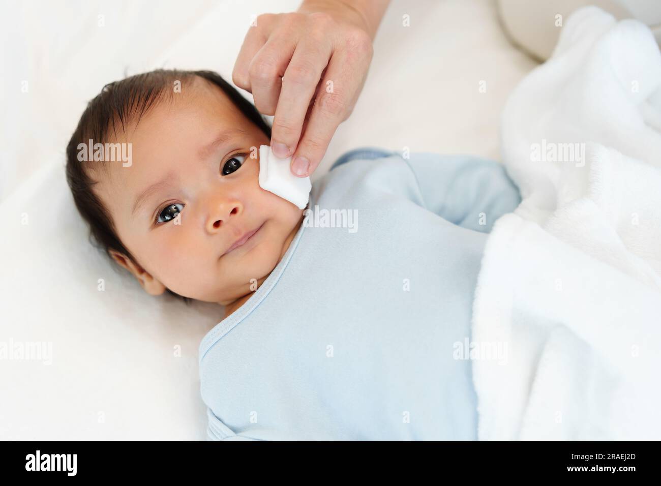 mother cleaning and wiping newborn baby face with cotton pad on a bed Stock Photo Alamy