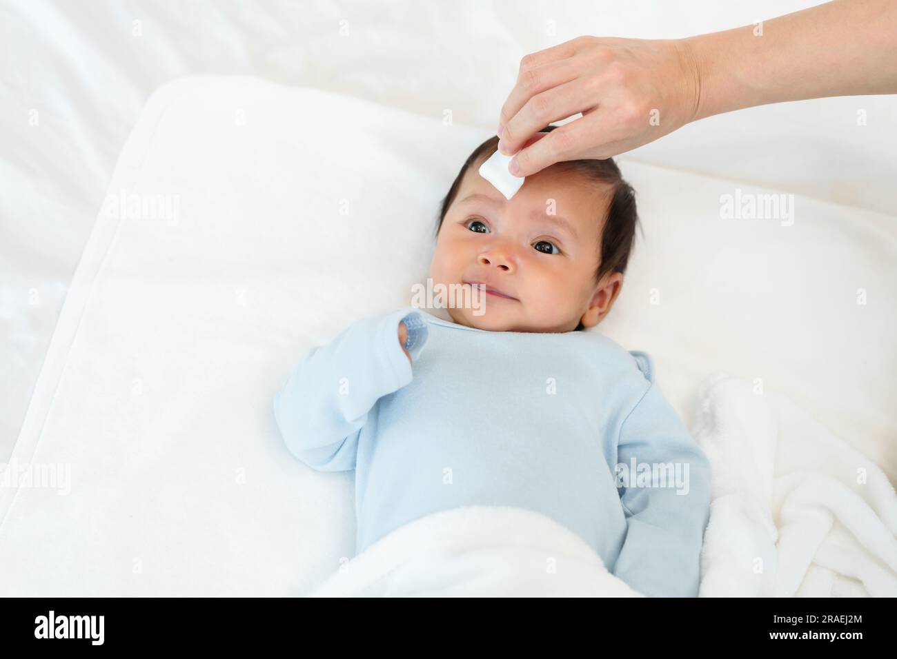 mother cleaning and wiping newborn baby face with cotton pad on a bed Stock Photo Alamy