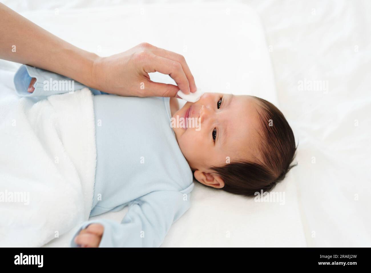 mother cleaning and wiping newborn baby face with cotton pad on a bed Stock Photo Alamy