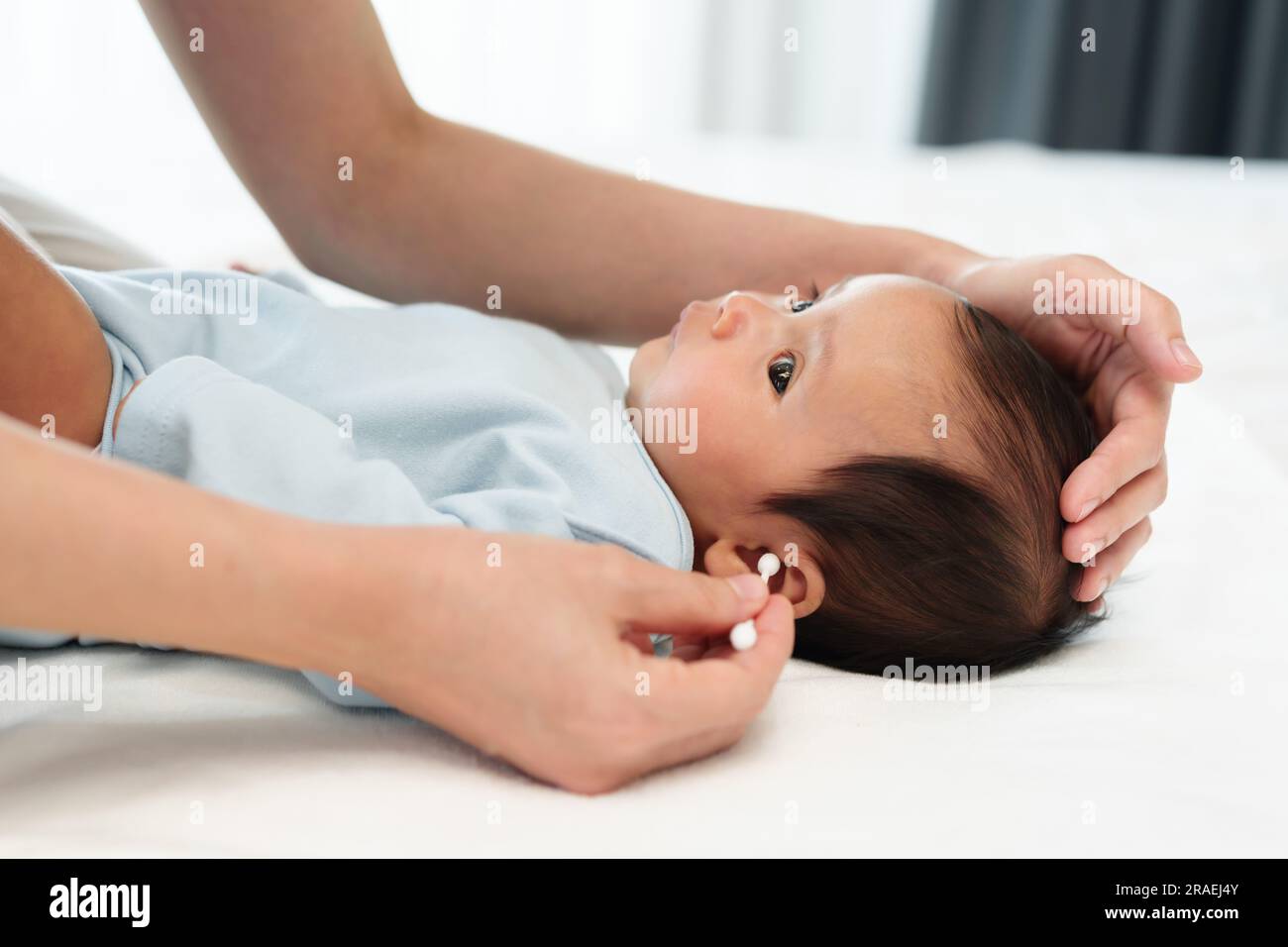 mother using cotton bud to cleaning ear of newborn baby on a bed Stock