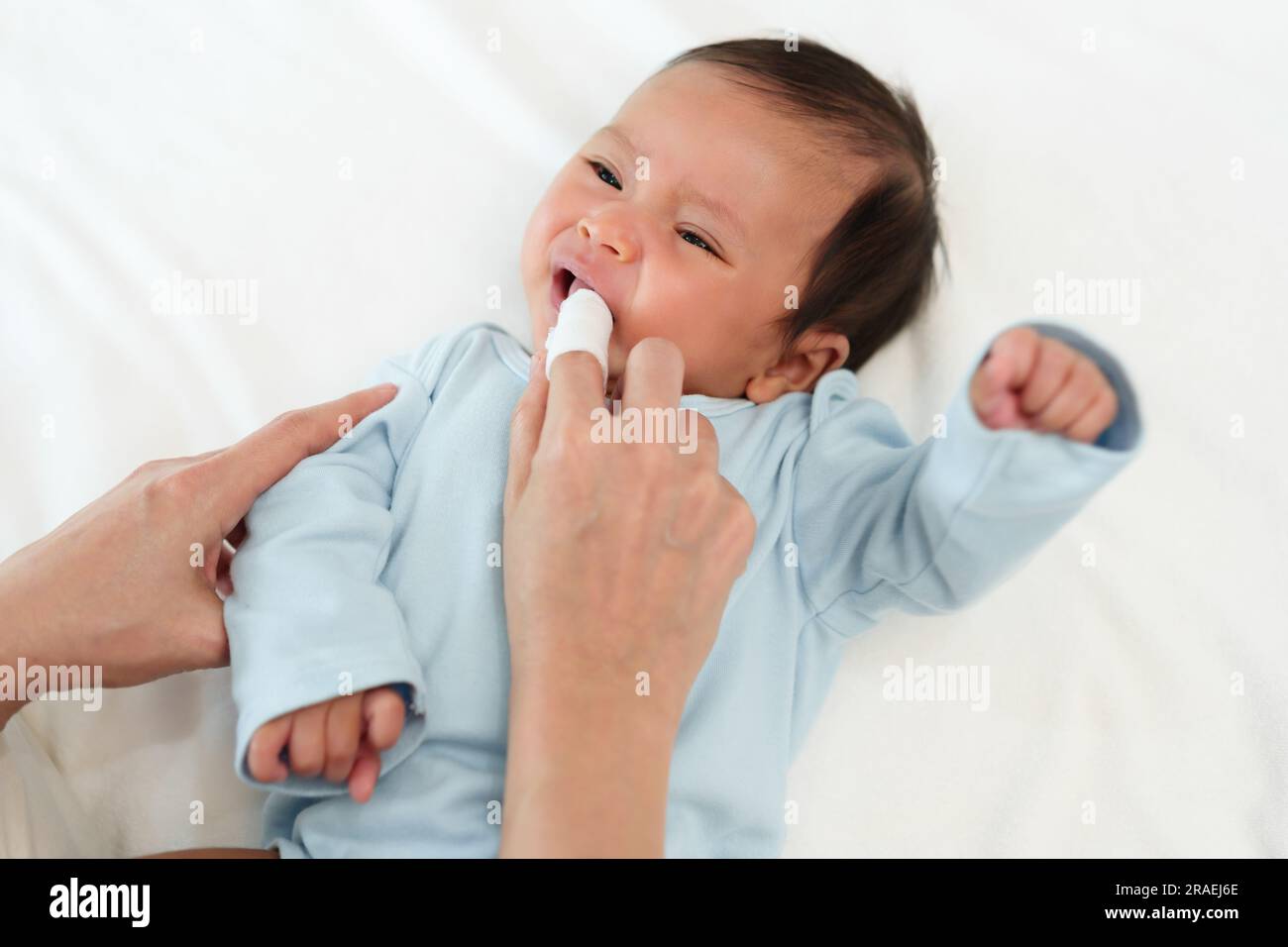 mother using finger to clean newborn baby mouth (tongue and gum) with clean gauze on a bed Stock Photo