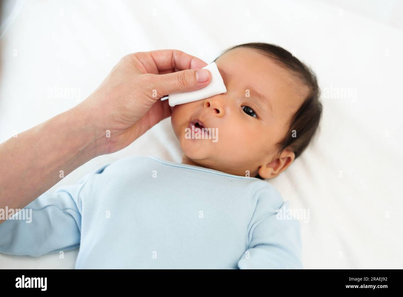mother cleaning and wiping newborn baby eye with cotton pad on a bed