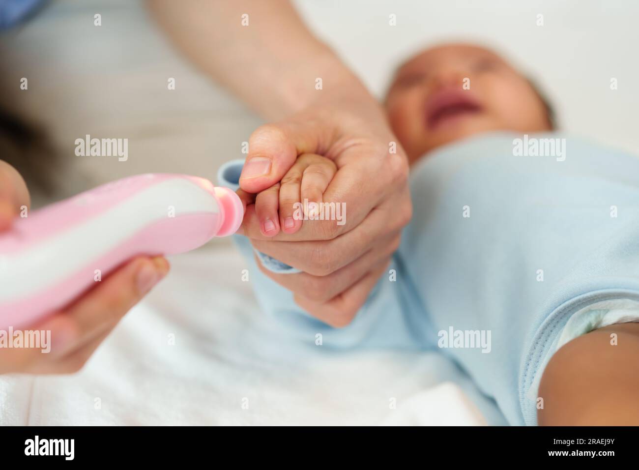 mother cutting newborn baby's fingernails with auto electic nail