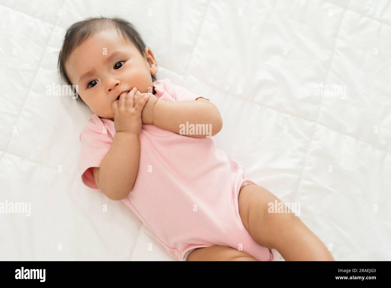 infant baby putting hands in mouth and sucking fingers on a bed Stock Photo