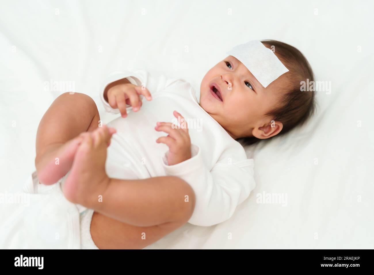 sick crying baby with cool fever jel pad on forehead Stock Photo