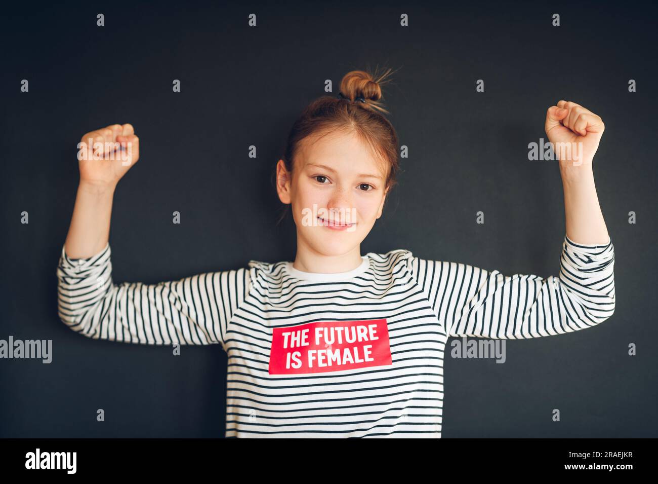 Studio shot of young strong preteen girl flexing arms muscles, wearing