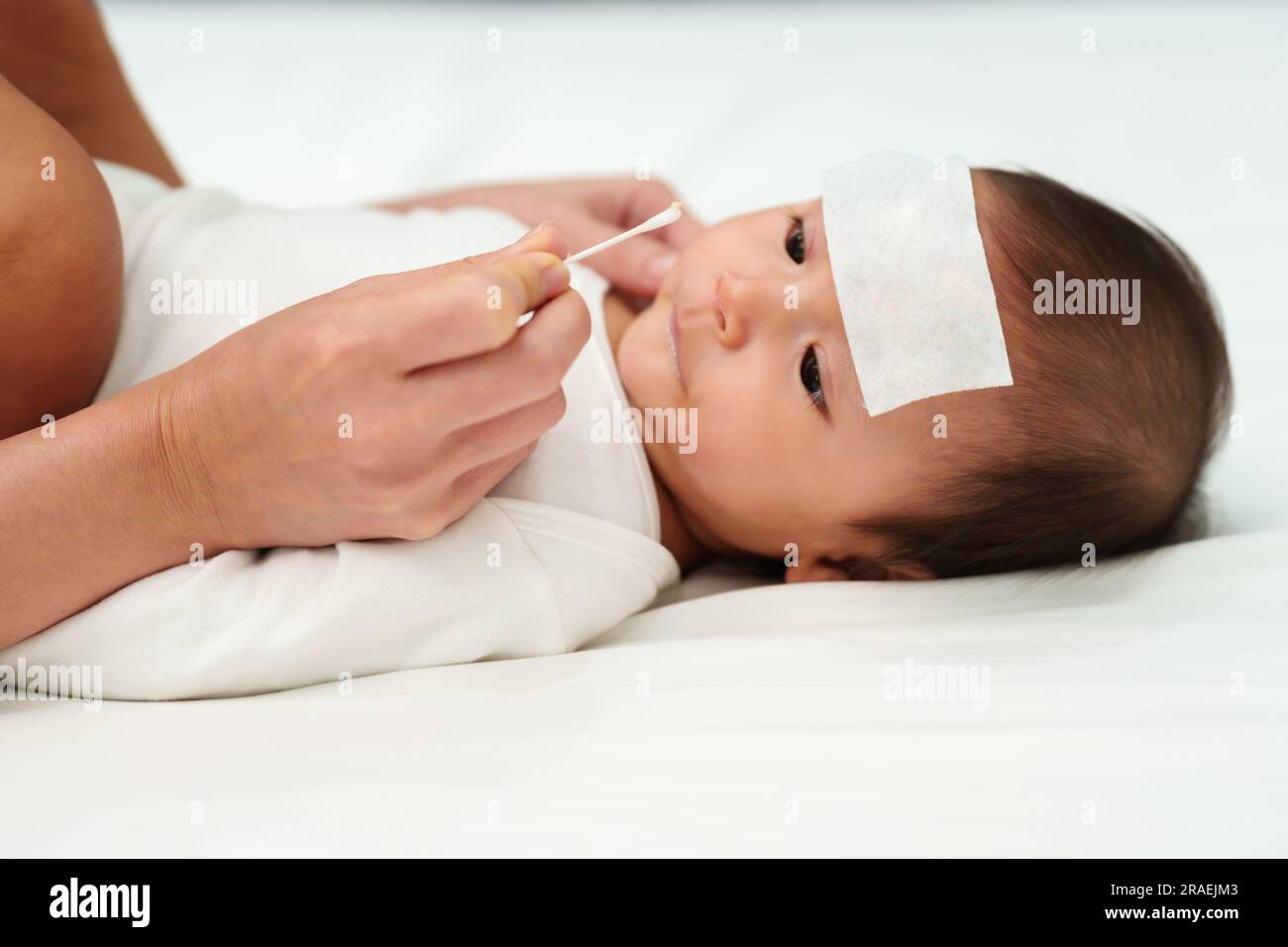 mother using cotton bud to clean nose of sick baby with cool fever jel