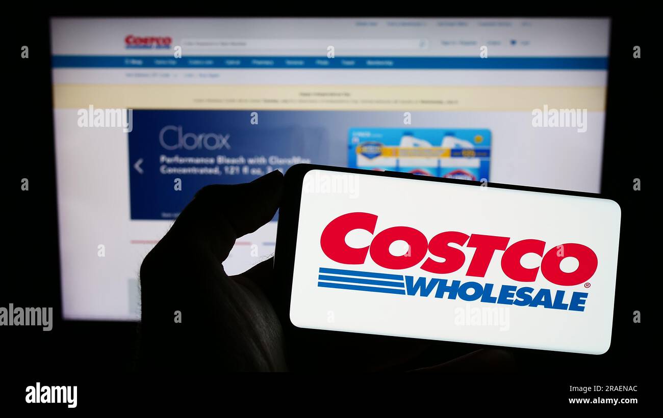 Person holding smartphone with logo of US company Costco Wholesale Corporation on screen in front of website. Focus on phone display. Stock Photo