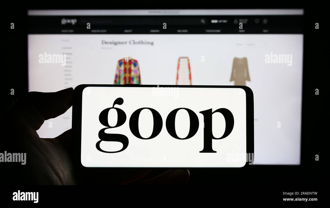 Person holding cellphone with logo of US publishing and e-commerce company Goop Inc. on screen in front of webpage. Focus on phone display. Stock Photo