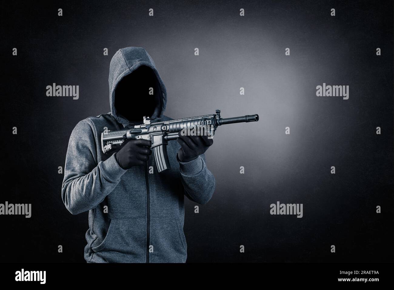 Hooded man with assault rifle over dark misty background Stock Photo
