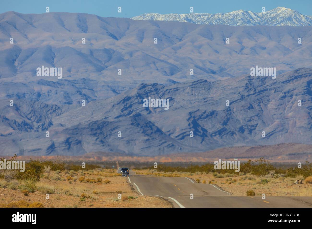 Teleaufnahme einer Strasse durch die Wüste von Arizona mit beeindruckendem Gebirgszug und schneebedeckten Gipfeln im Hintergrund fotografiert in den U Stock Photo