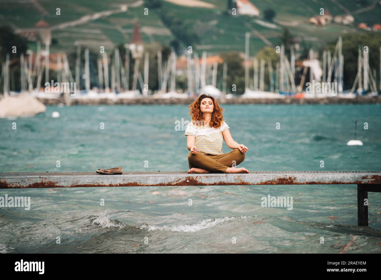 Young beautiful woman in lotus position meditating on the lake side on a srormy day Stock Photo