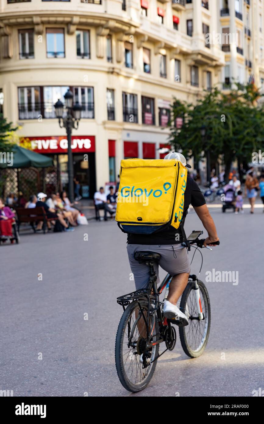 Valencia, Spain - June, 2023: Glovo rider, deliveryman on a bicycle going to deliver an order. Glovo app delivery service Stock Photo