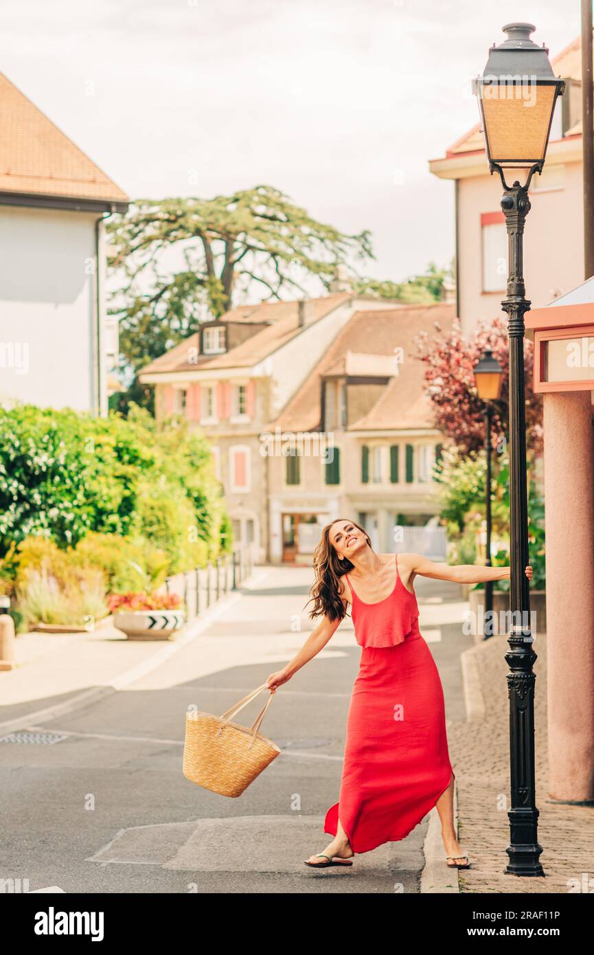 Summer portrait of happy woman with beautiful hair style, wearing red dress, walking down the street Stock Photo