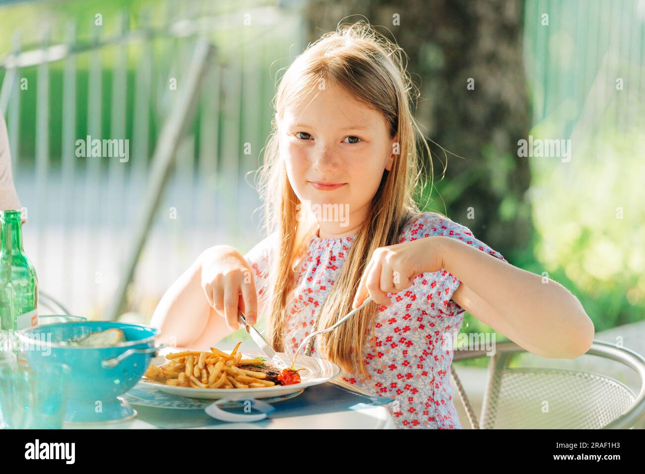 Little girl eating dinner on a terrace in outdoor restaurant Stock Photo