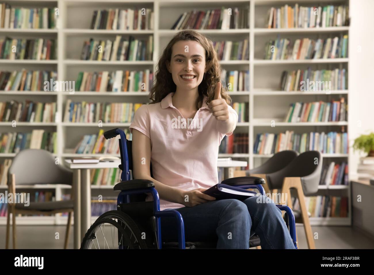 Happy pretty student girl using wheelchair, posing in library Stock Photo