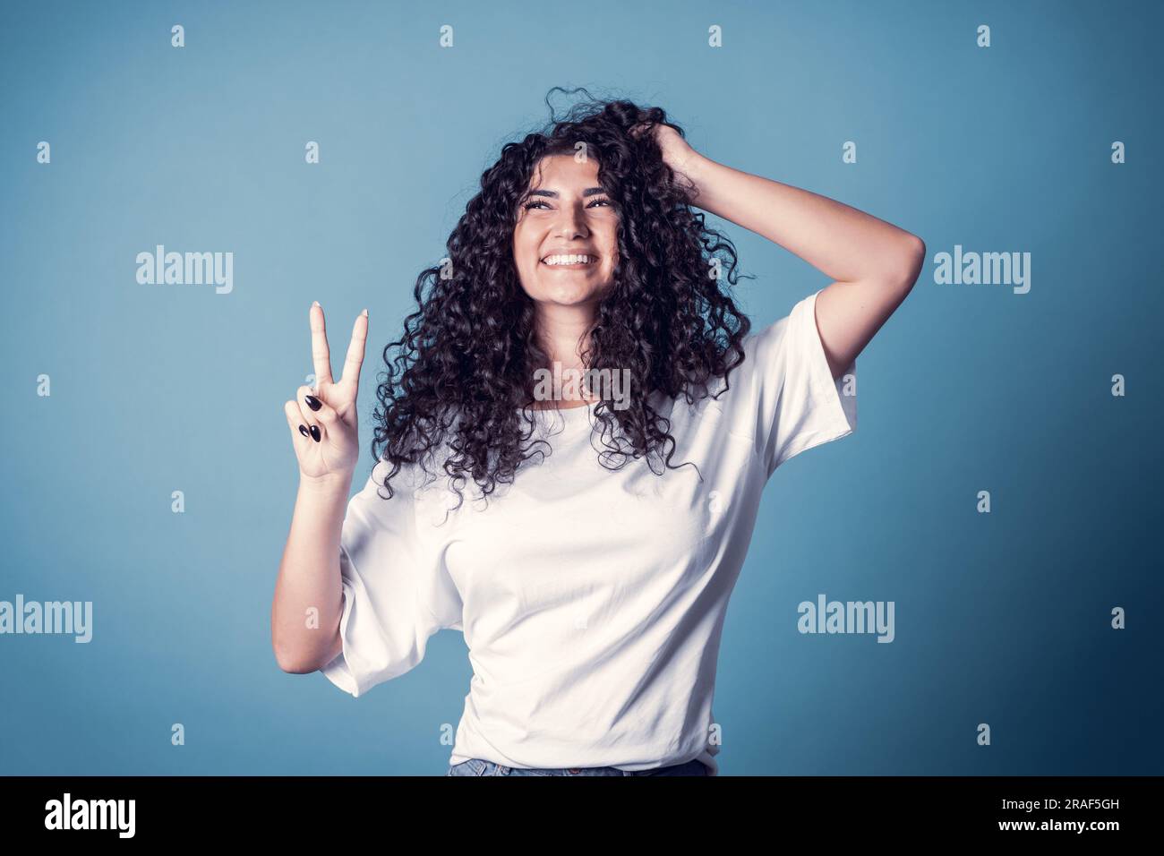 Shot of happy confident curly woman with toothy smile, wears casual basic solid white t-shirt, expresses good emotions, enjoys nice day, isolated over Stock Photo