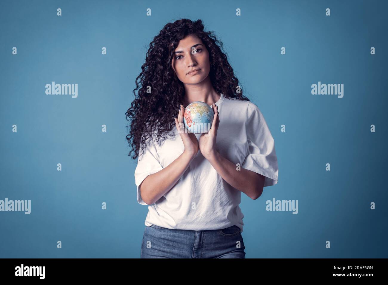 Studio shot of beautiful confident caucasian curly model woman wears blue jeans and casual basic solid white t-shirt, isolated over blue background. P Stock Photo