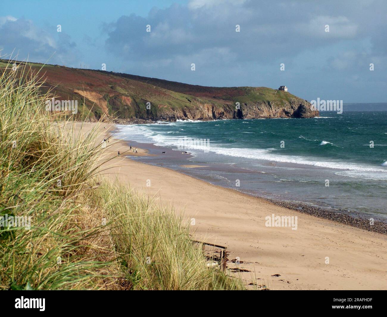 Bright autumn sunshine lights up the Cornish coast at Praa sands.The view over the grass, sand and cliffs to the house on Rinsey Head with the waves i Stock Photo