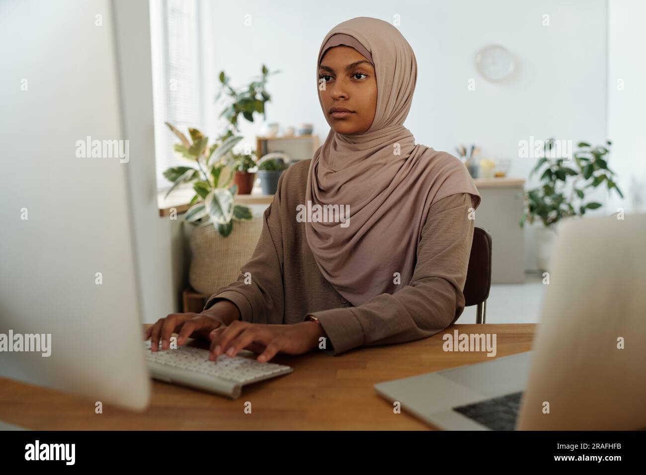 Young serious female programmer looking at computer screen while analyzing or decoding data or developing new software by workplace Stock Photo