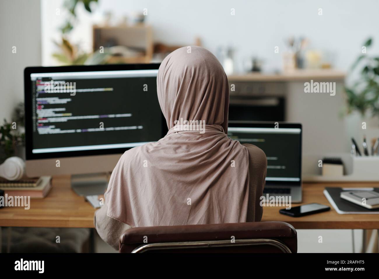 Rear view of Muslim female programmer in hijab sitting in front of ...