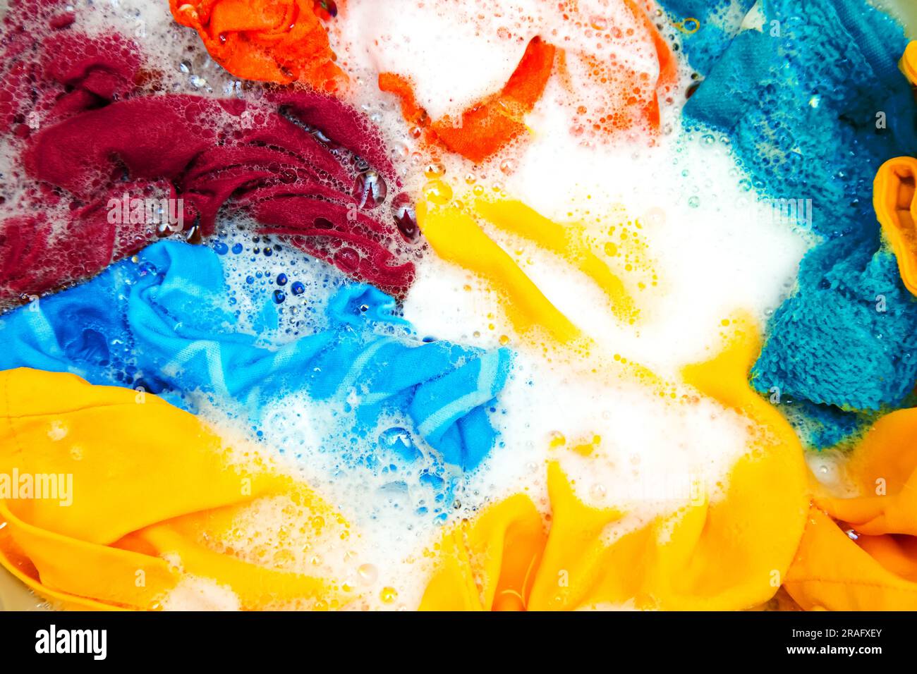 Colored clothes soaked in water with detergent and foam bubbles