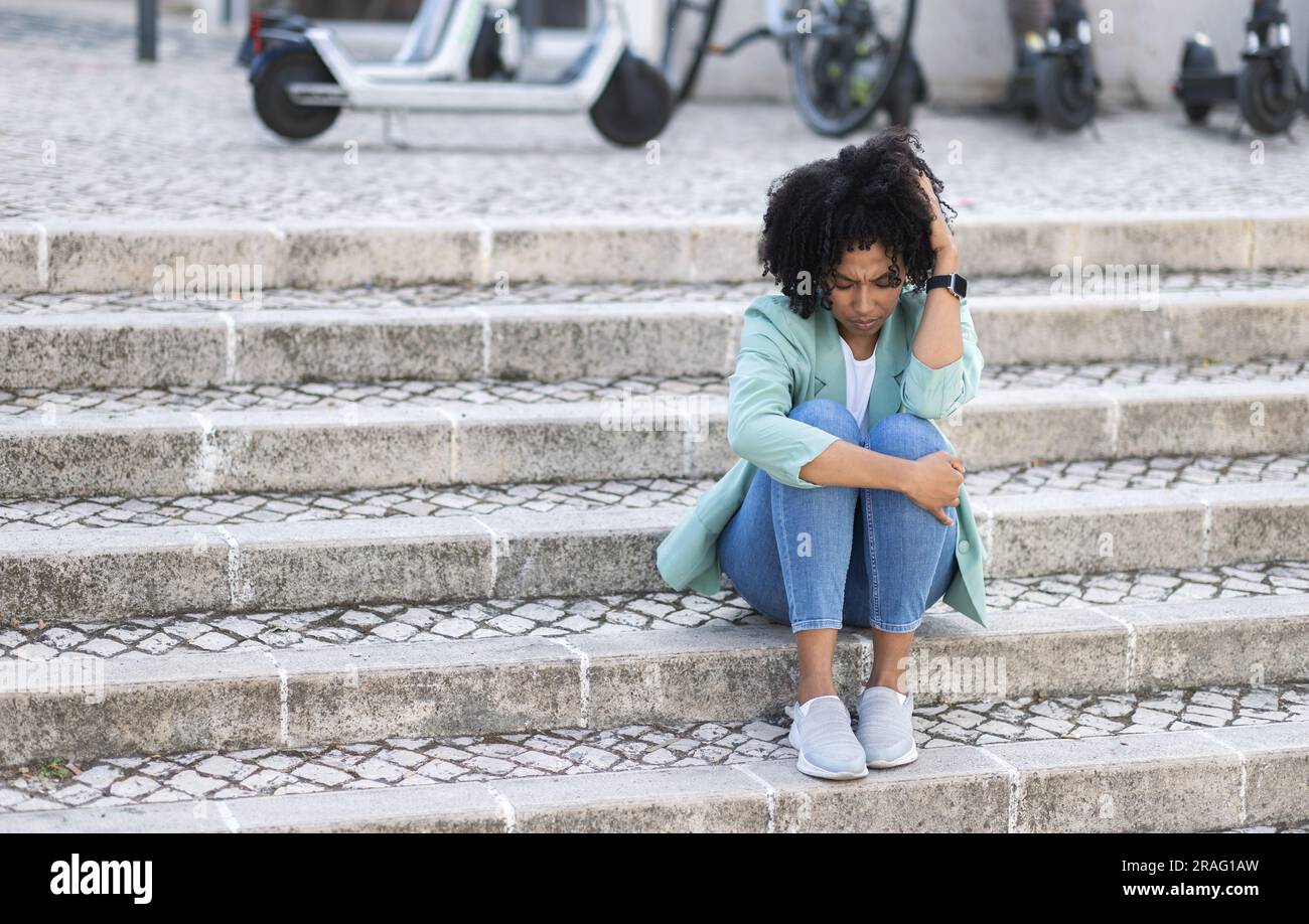 Upset broken young african american woman sitting on street Stock Photo