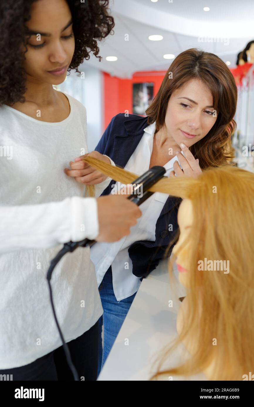 trainee hairdresser practicing using straighteners on a mannequin Stock Photo Alamy