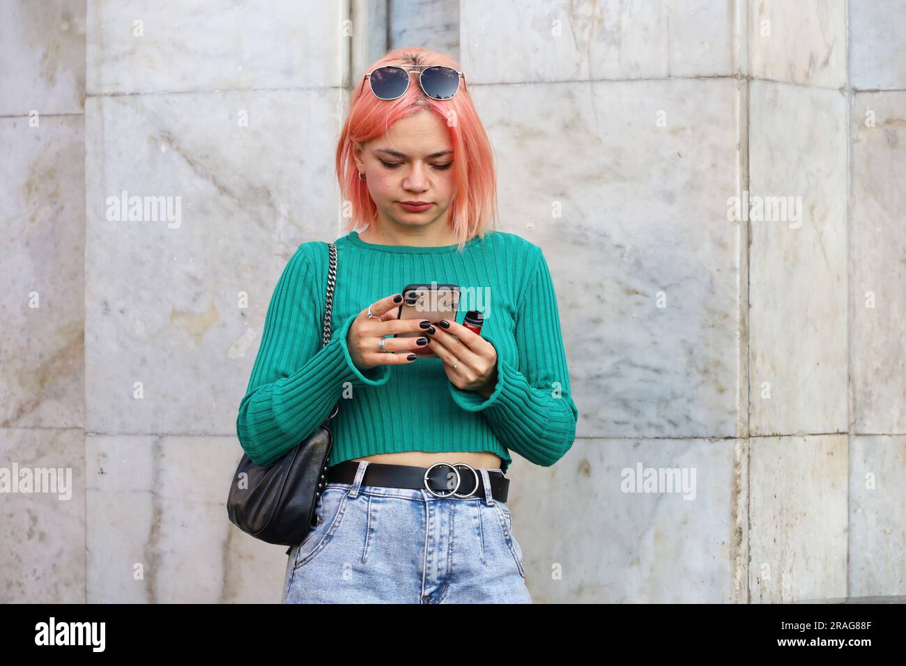 Slim girl with pink dyed hair standing on a street with smartphone. Using mobile phone in summer city Stock Photo