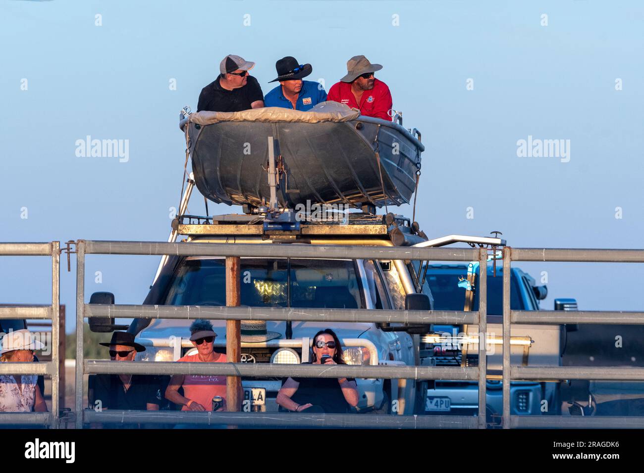 Three men in a dinghy mounted on the roof of a car watching a rodeo, Brunette Downs ABC Amateur Bush races,Northern Territory, NT, Australia Stock Photo
