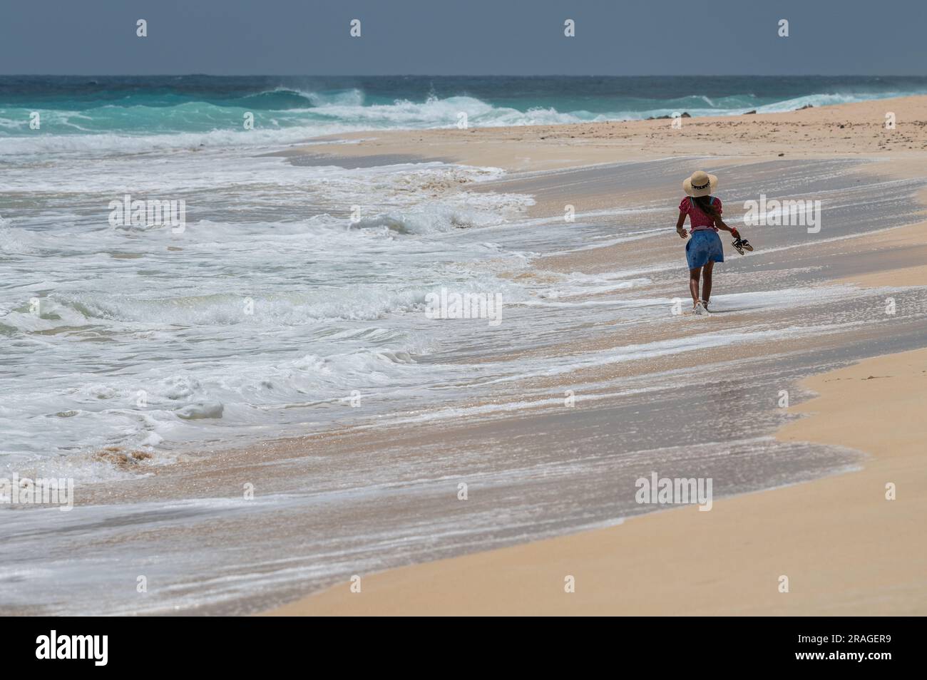 A young tourist woman walks along the sand during a hot summer day at ...