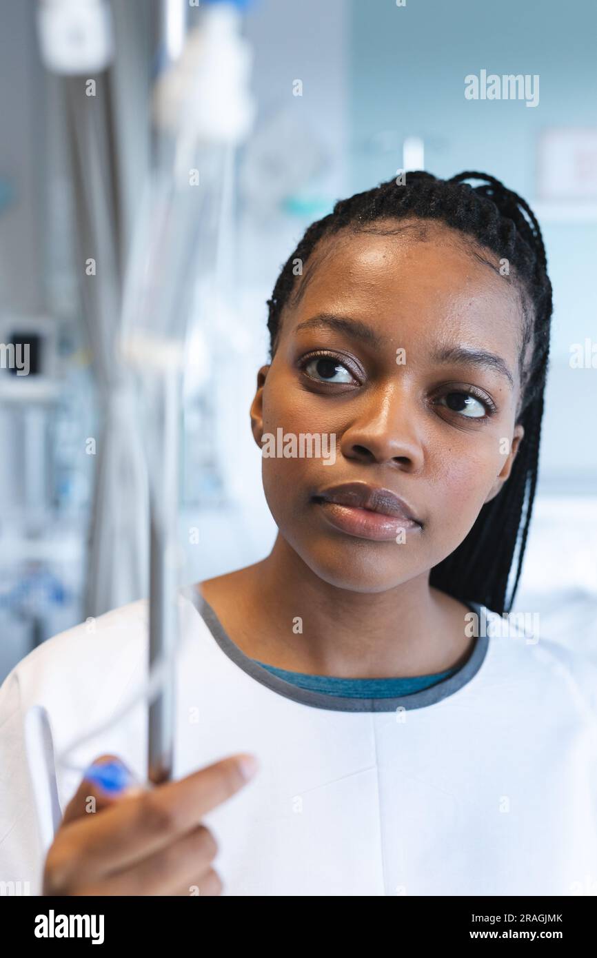 African american female patient wearing hospital gown, holding drip in ...