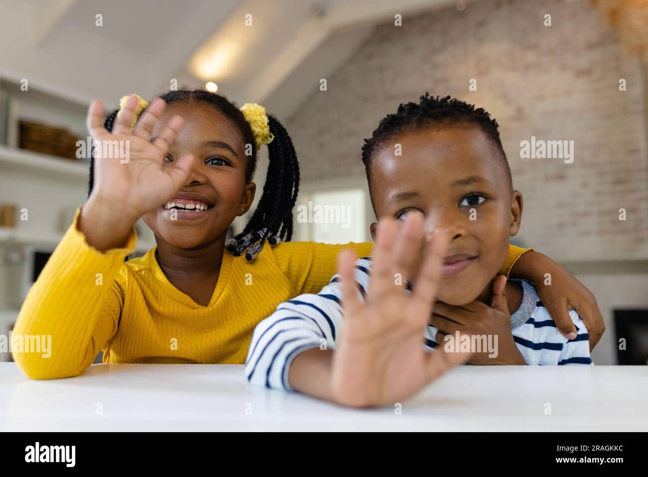 Portrait of smiling african american boy and girl waving hands while studying online at home Stock Photo