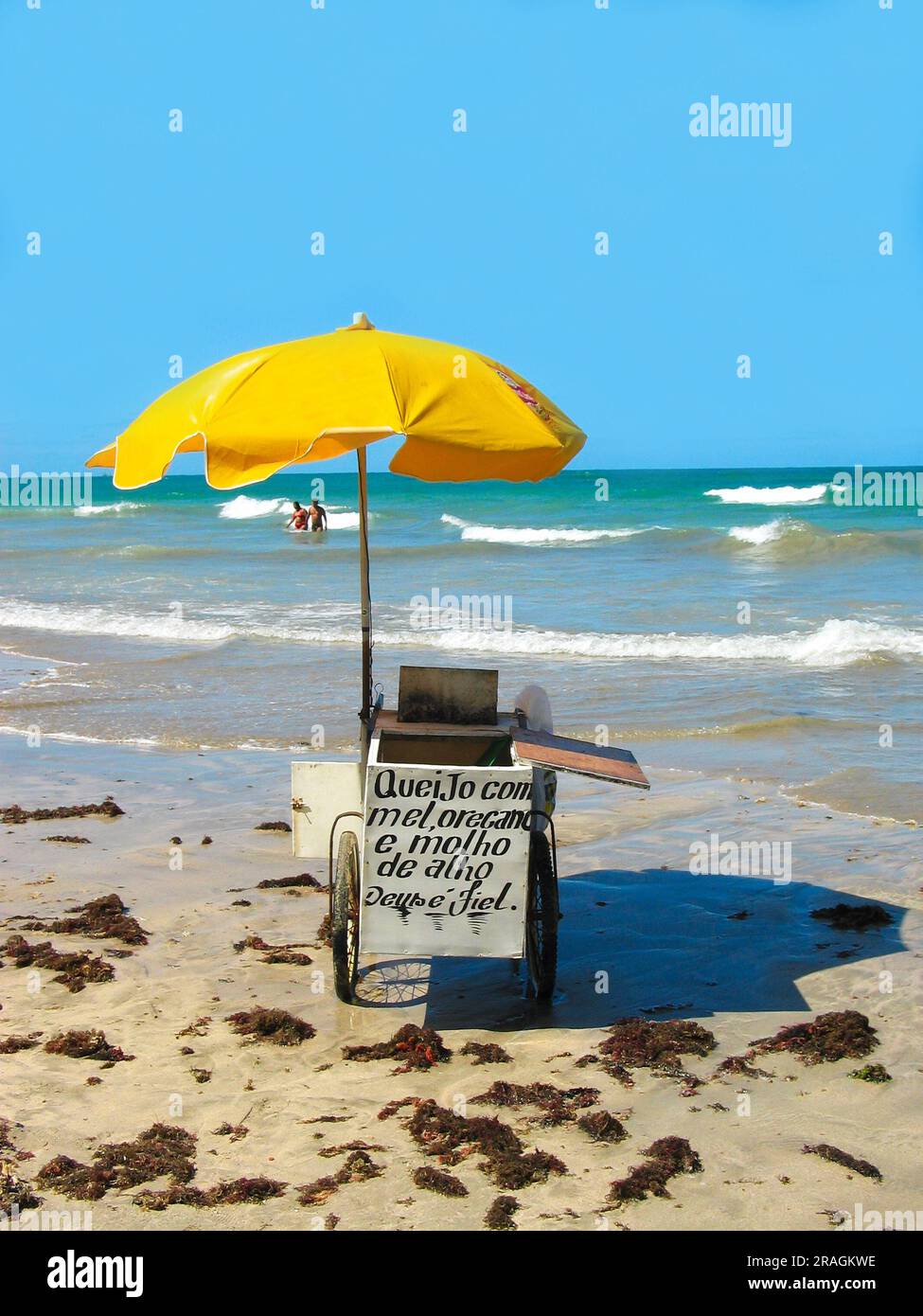 Beach in Brazil, yellow parasol beach troley. / Text in Portuguese 'Queijo com mel, oregano e molho de alho Deus e fiel'  (English: Cheese with honey, Stock Photo
