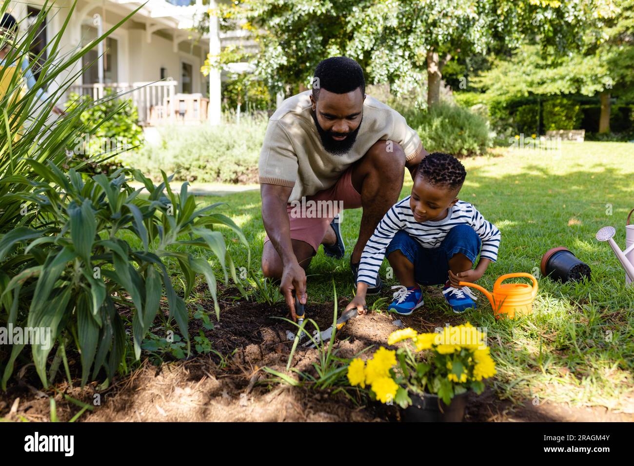 African american father and son digging dirt with tools on grassy field in backyard Stock Photo