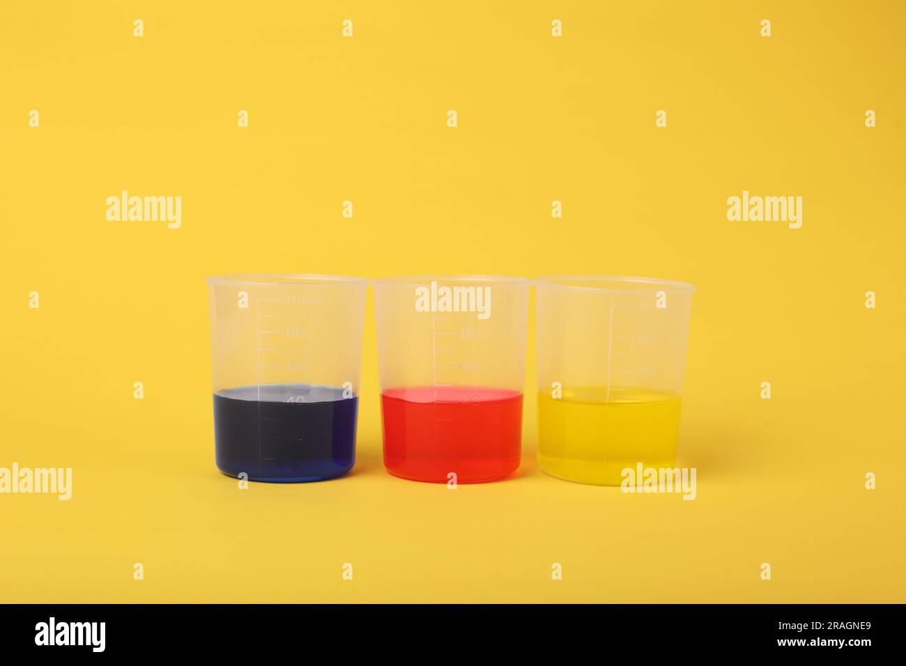 Beakers with colorful liquids on yellow background. Kids chemical experiment set Stock Photo